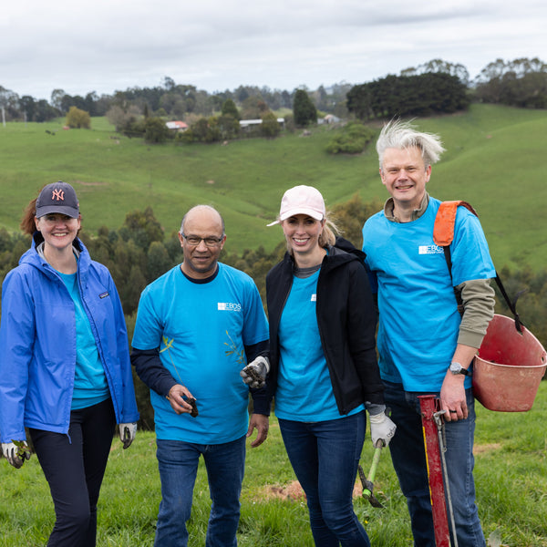 Group of five people in blue shirts standing in a field with green hills and trees in the background.