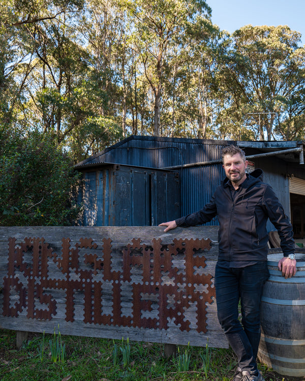 Man standing next to a barrel with 'Kinglake Distillery' sign in a rustic setting