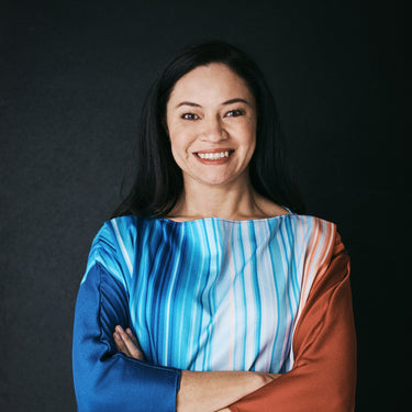 Woman wearing a colorful striped shirt with arms crossed against a black background