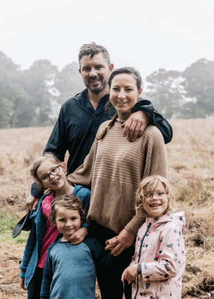 Family of five standing in a field with trees in the background